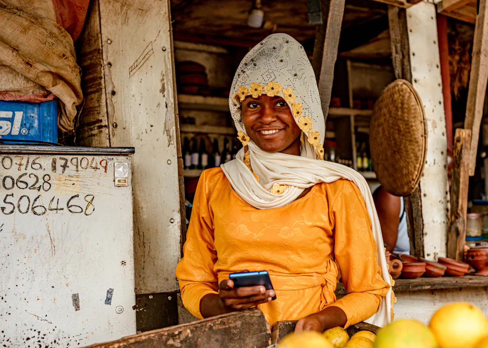 Commerçante souriante, téléphone à la main, derrière son étal